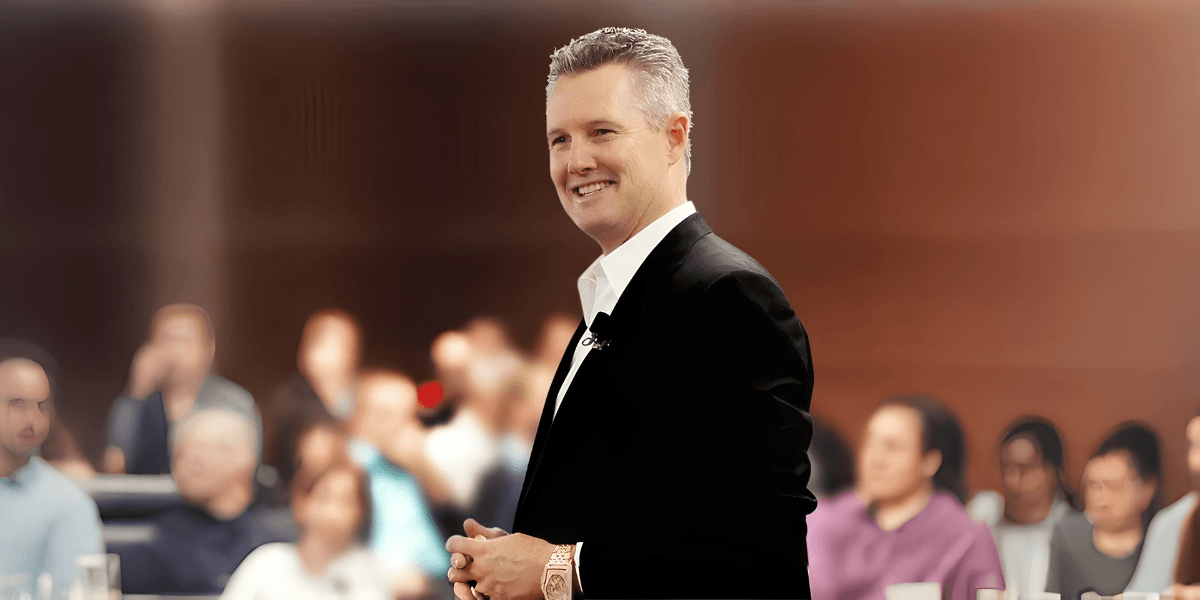 Smiling speaker in a suit addressing an audience in a conference setting