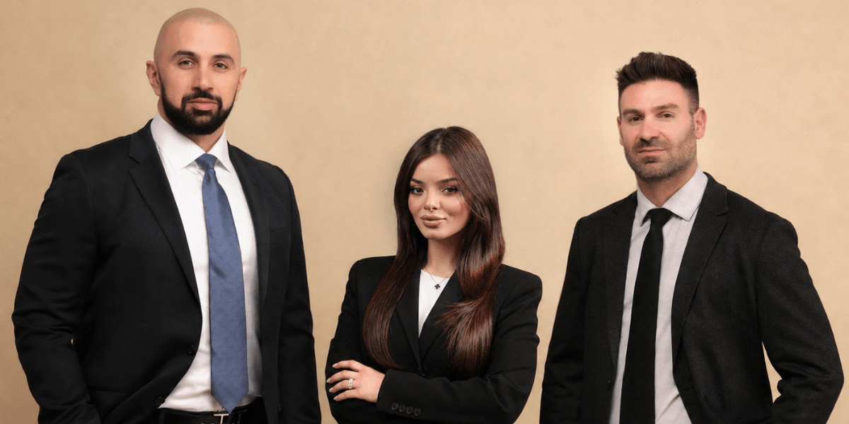 Three professionals in formal attire standing together against a neutral background