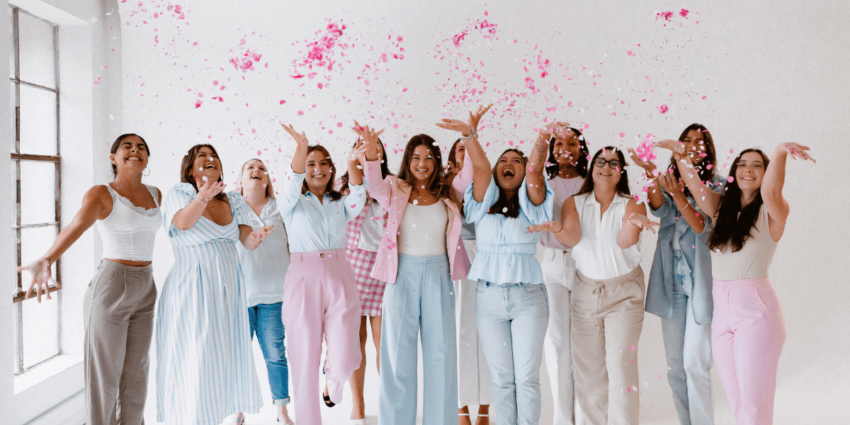 A group of joyful women throwing pink confetti in a bright, cheerful setting