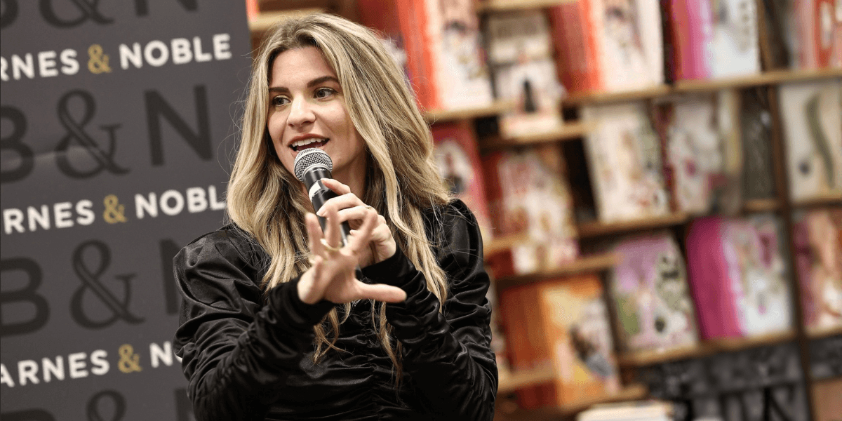 A woman with long hair speaking into a microphone at a bookstore event