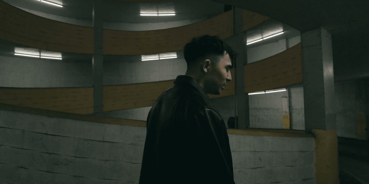 A person in a leather jacket stands in a dimly lit parking garage.