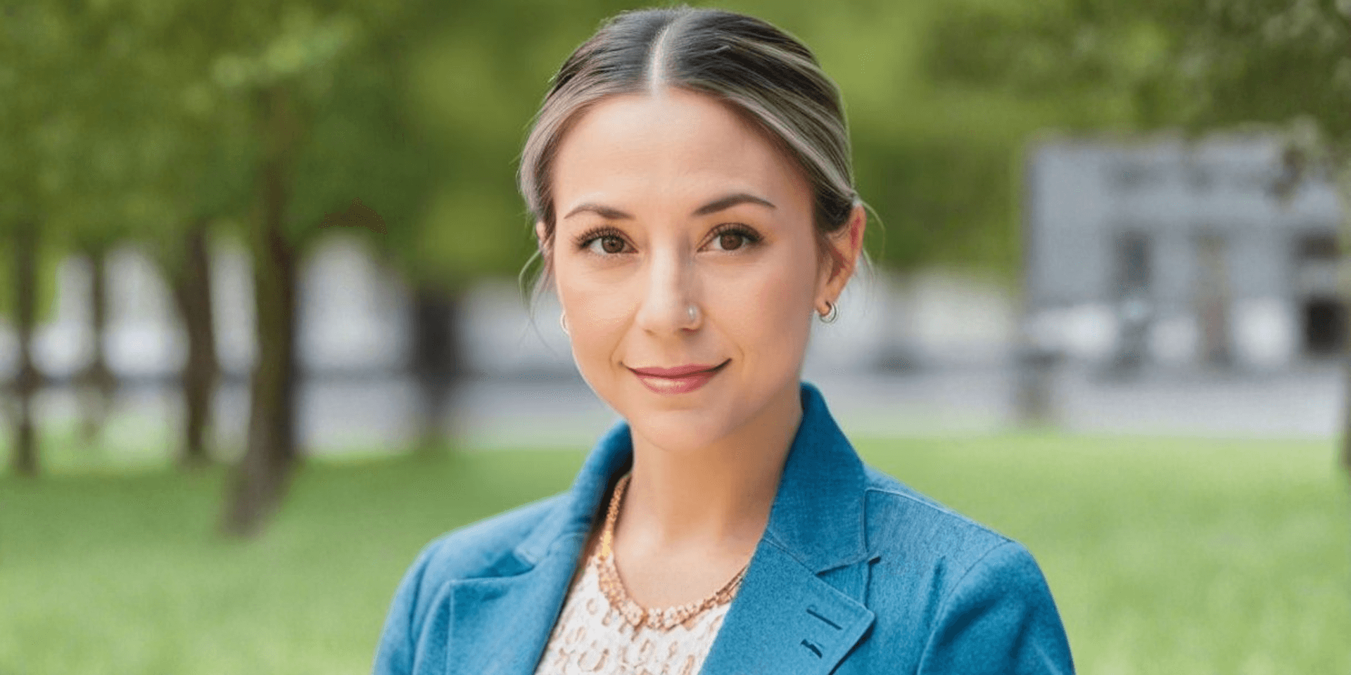 Woman with a light blue blazer and gold necklace in a green park setting