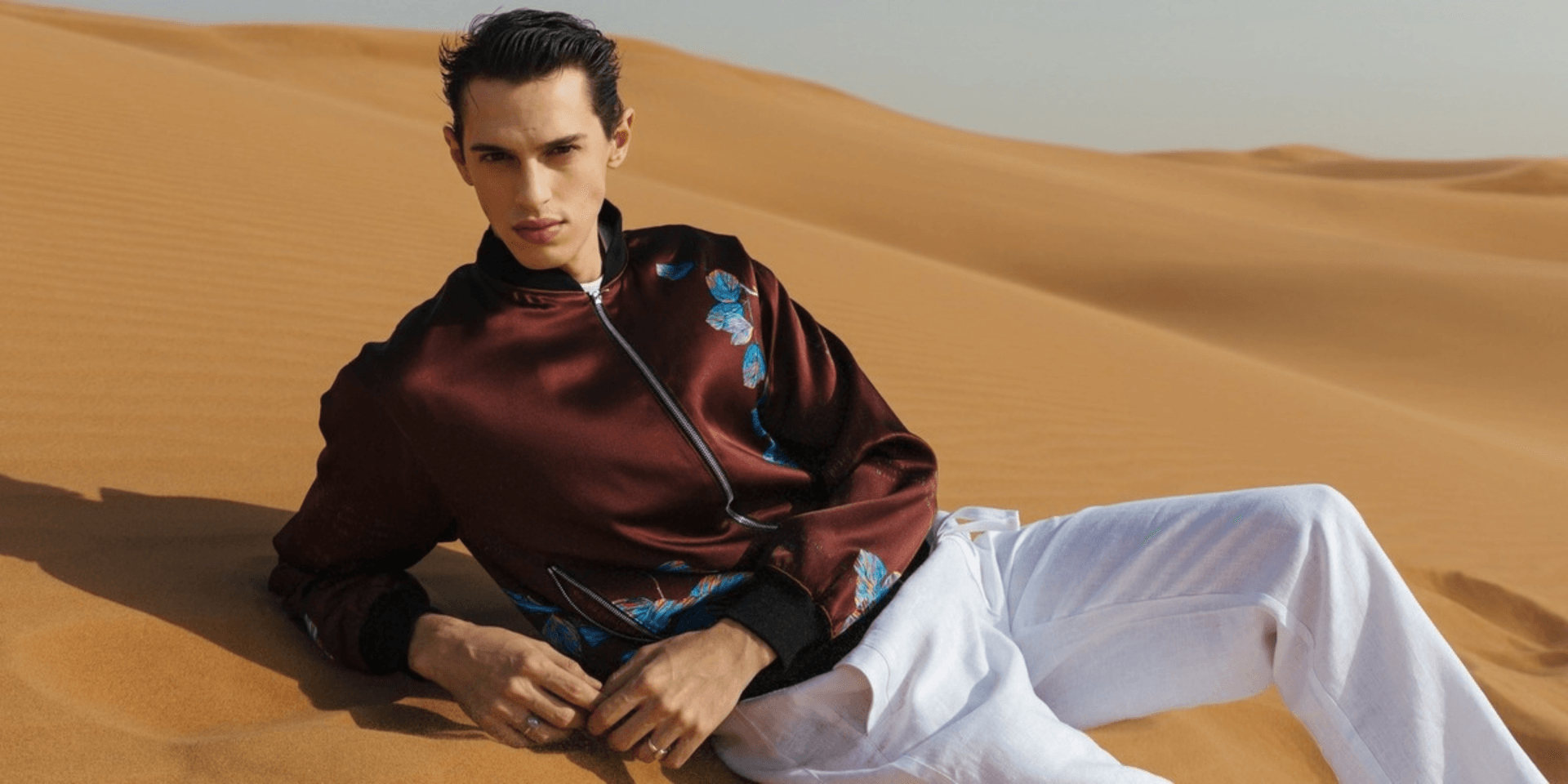 Male model in a desert wearing a patterned bomber jacket and white pants